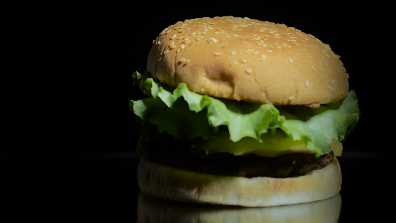 deliciosa hermosa hamburguesa girando en una superficie de espejo en un fondo negro con lugar para escribir. 4k