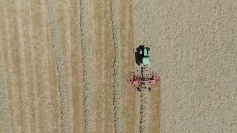 drone tracking view of a green tractor pulling a large grass harvester across a freshly cut field, emphasizing the efficiency of modern farming practices