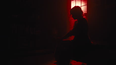 woman sits on sofa as red light silhouettes her from window