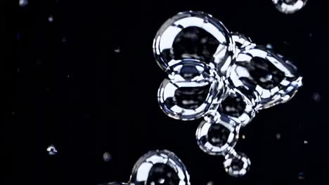 iridescent spherical bubbles ascending gracefully against deep black background, reflecting surrounding light with metallic shimmering surfaces and demonstrating fluid dynamic motion