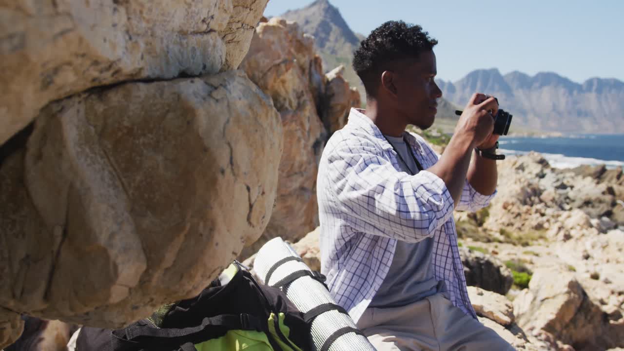 hombre afroamericano haciendo senderismo en el campo tomando fotos por la costa