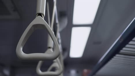 the hand ring  in the train carriage. the train is moving and the camera shakes slightly. the subject is on the left. there are lights in the background.