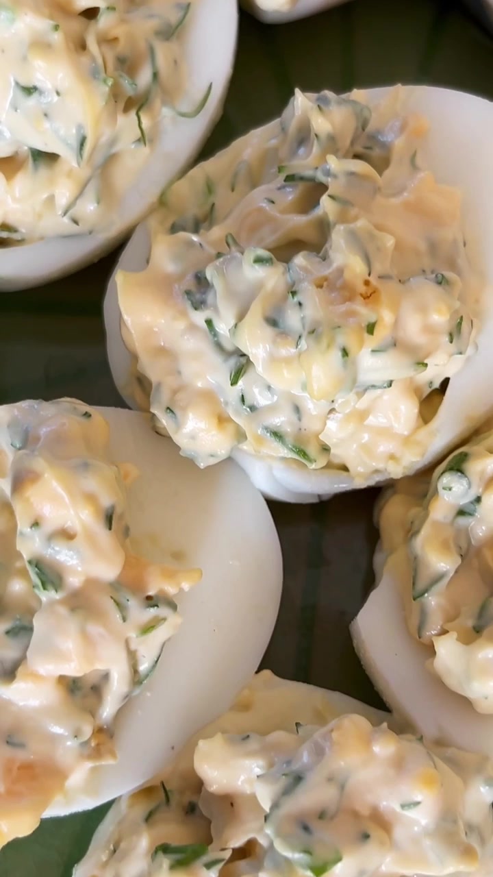 Macro close-up of creamy deviled eggs with herb-speckled filling, styled as a rich homemade appetizer on a serving platter for brunch or holiday entertaining.