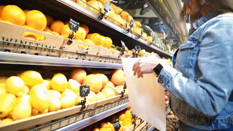 happy woman buying fresh fruits and vegetables and putting them in a paper bag in a grocery store or supermarket. healthy lifestyle.