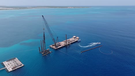 Aerial-orbiting-shot-of-private-boat-leaving-new-port-terminal-during-building-phase-surrounded-by-blue-sea-in-Pedernales,-Dominican-Republic