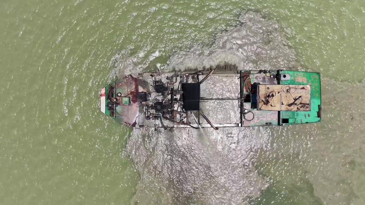Ripresa aerea dall'alto direttamente sopra una draga per sabbia, una pallida scia di sedimento che si diffonde a valle dallo scarico, bacino idrico di Dau Tieng, Tay Ninh, Vietnam