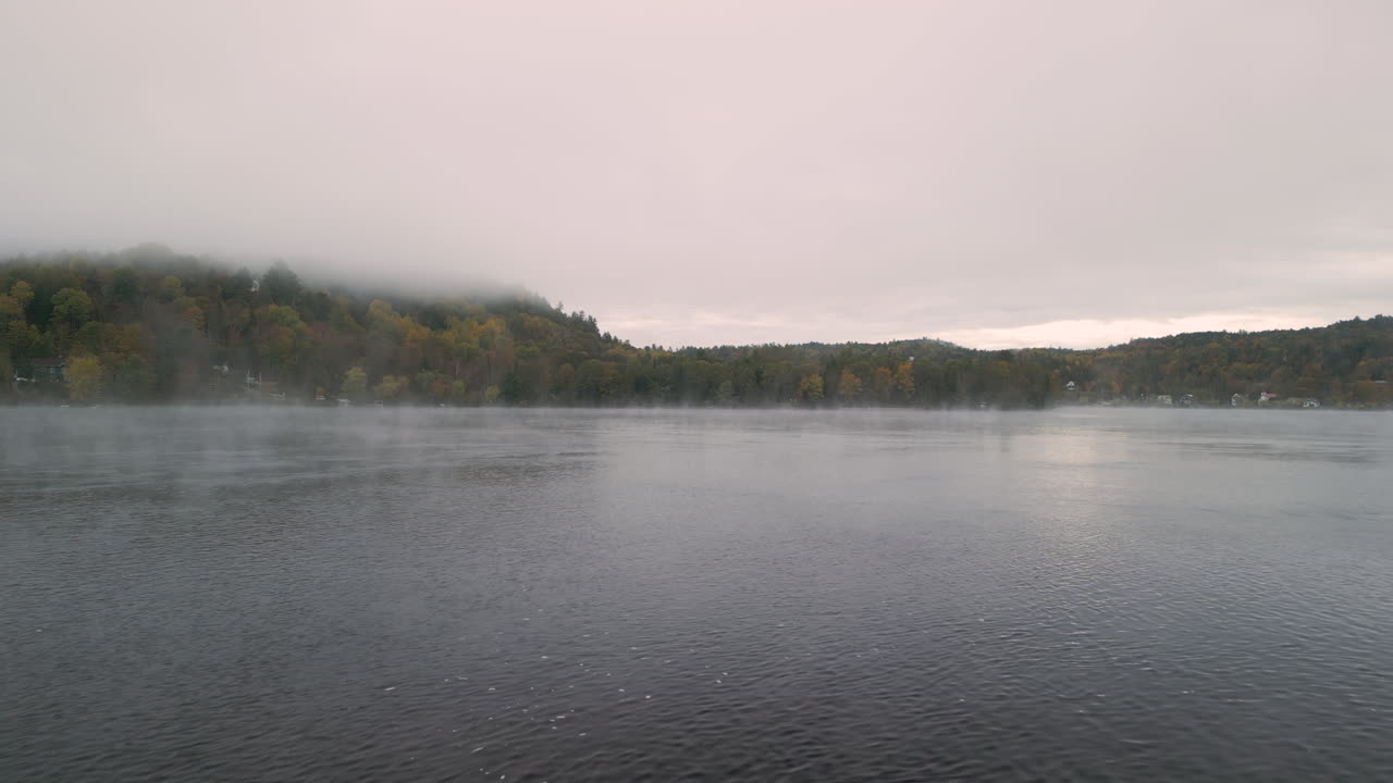 A drone flies over a quiet misty river in the fall season