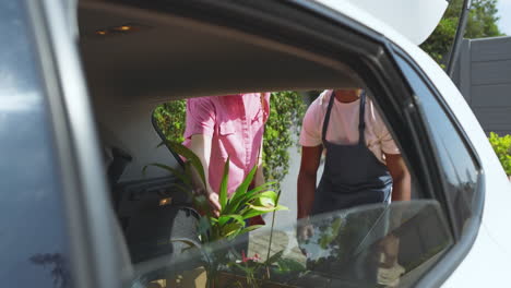man in apron discussing gardening tips with woman near car in driveway, in greenhouse