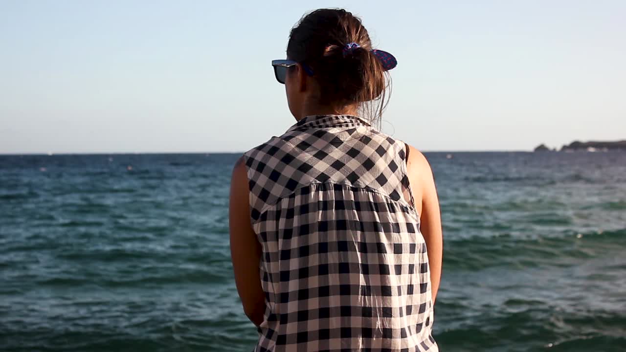 Medium shot of the back of a girl looking at the waves of the ocean