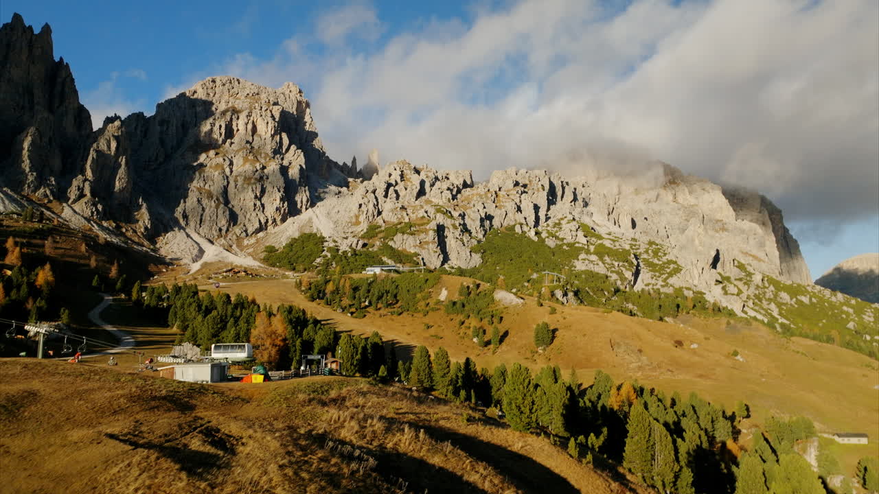 Vista aerea di un'idilliaca stazione sciistica che si affaccia su alte montagne rocciose e pini in Val Gardena, Dolomiti, durante l'estate.