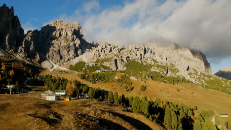 Aerial-view-of-idyllic-ski-resort-facing-tall,-rocky-mountains-and-pine-trees-in-Val-Gardena,-Dolomites-during-summer