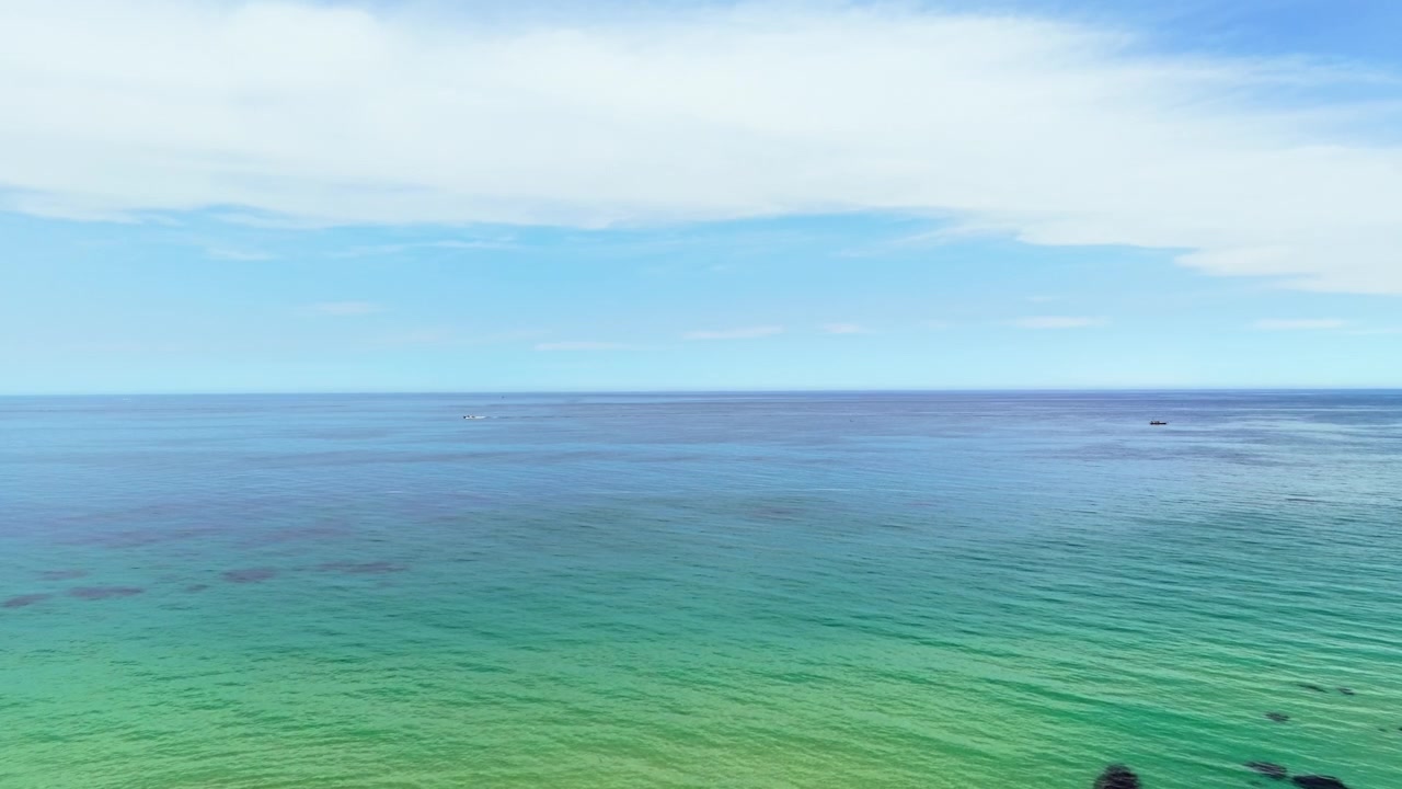 Vaste acque turchesi dell'oceano si estendono verso l'orizzonte con barche in lontananza vicino a Gangneung, sulla costa del Mar Orientale della Corea del Sud.