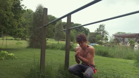 young fit topless man stretches wrists before exercising on parallel bars at home gym