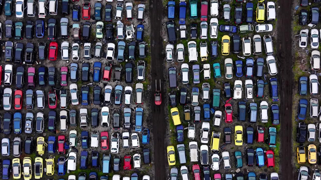 Schema aereo di automobili rottamate. Griglia ripetitiva di auto ammaccate in colori tenui separate da due strade di accesso sterrate e diritte