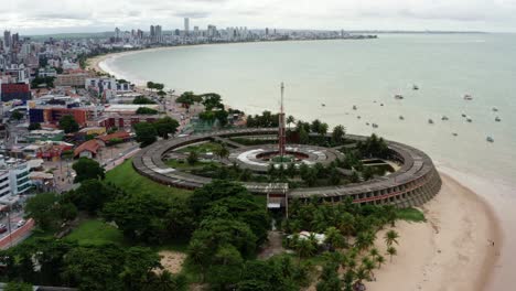 Rotating-aerial-drone-shot-of-a-large-round-building-on-the-beach-in-the-colorful-tropical-beach-capital-city-of-Joao-Pessoa-in-Paraiba,-Brazil-from-the-Tambaú-neighborhood-on-an-overcast-morning