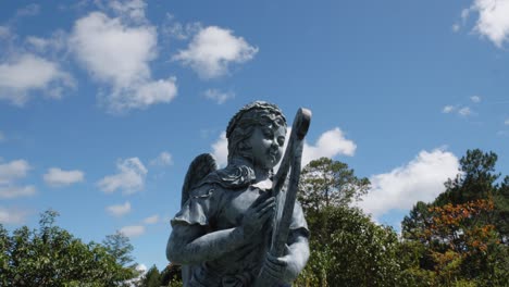 escultura de arcilla de un ángel con un arpa, sobre un fondo de cielo azul