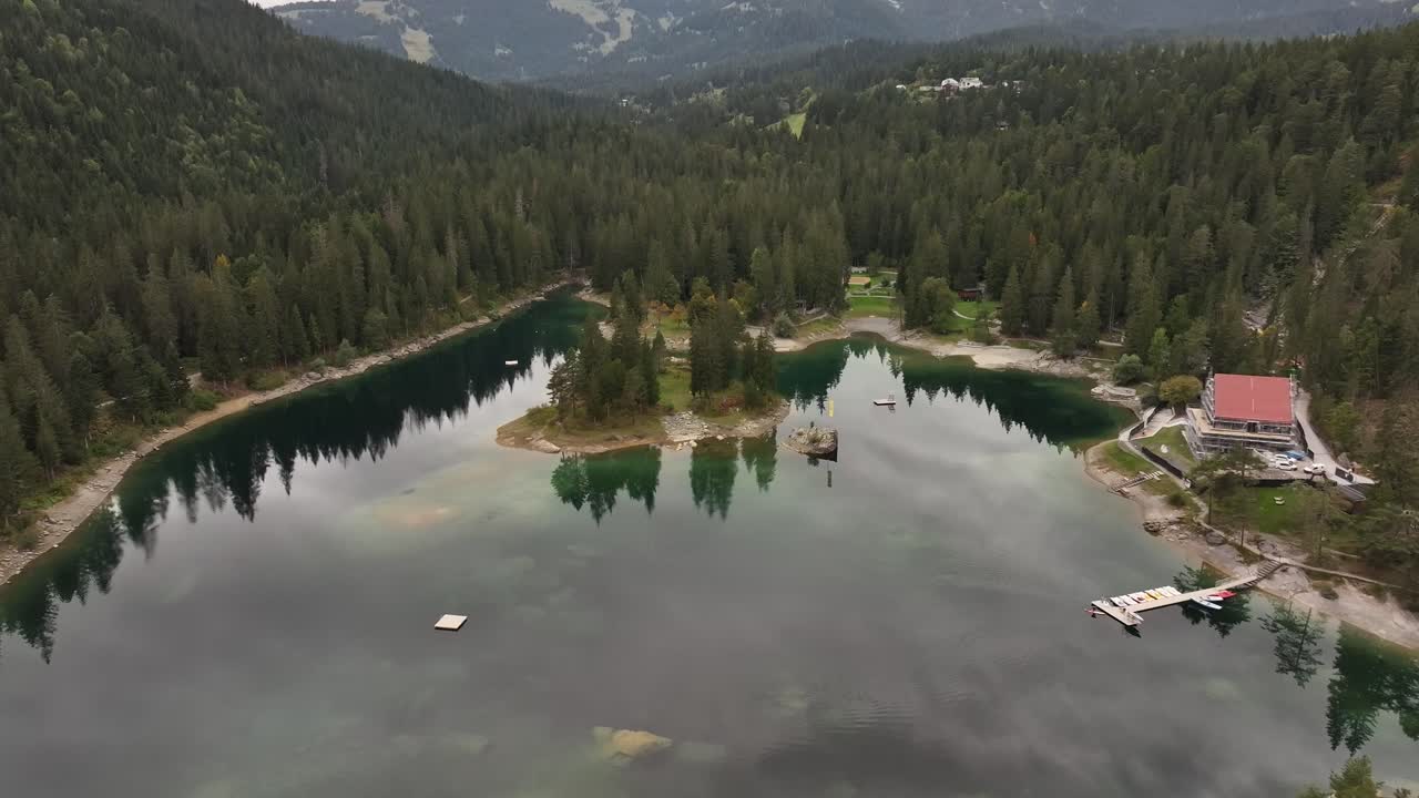 Stunning reveal shot of Lake Caumasee near the village of Flims, Switzerland, showcasing the crystal-clear waters surrounded by dense forests and towering trees. Aerial view.