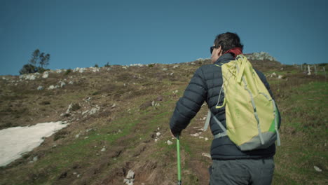 cámara rastreando a un excursionista masculino con una mochila verde claro y bastones de senderismo verdes en un camino cuesta arriba en la montaña ratitovec