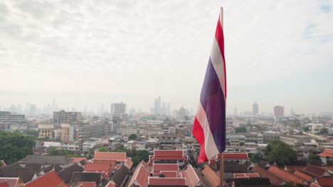 4k thailand state flag fluttering in the wind on the top of wat saket golden mountain with bangkok at the background