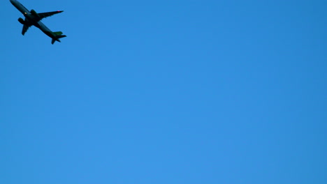 Silhouetted-passenger-jet-airplane-taking-off-against-blue-sky---low-angle-view-from-wire-fence-of-aerodrome