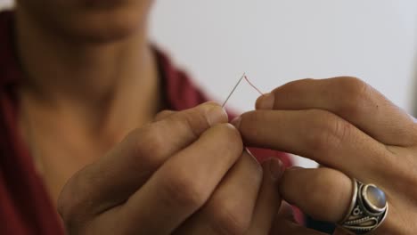 middle eastern woman trying to thread unsuccessfully a red thread in the eye of a needle