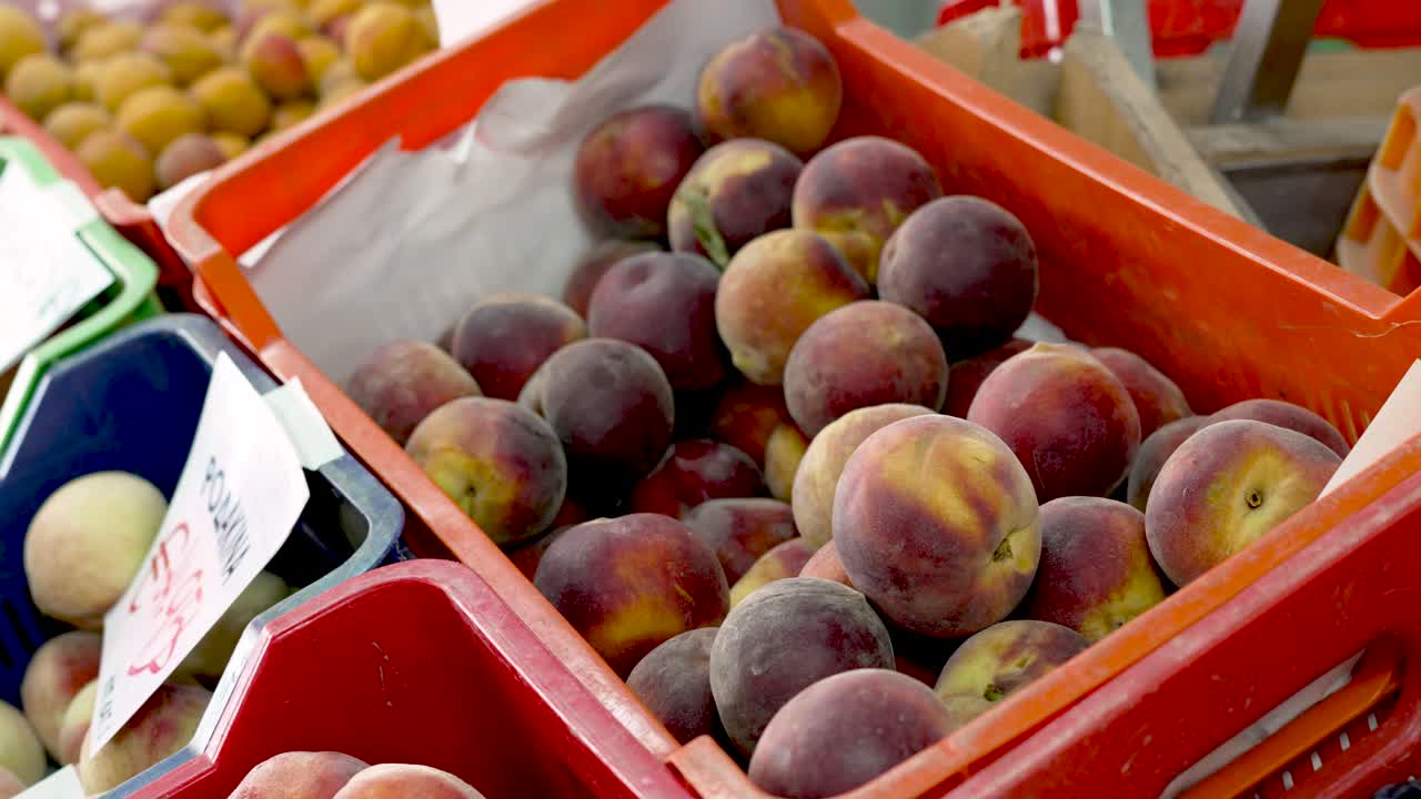 Fresh, juicy peaches fill a bright orange crate, drawing attention in a lively market scene