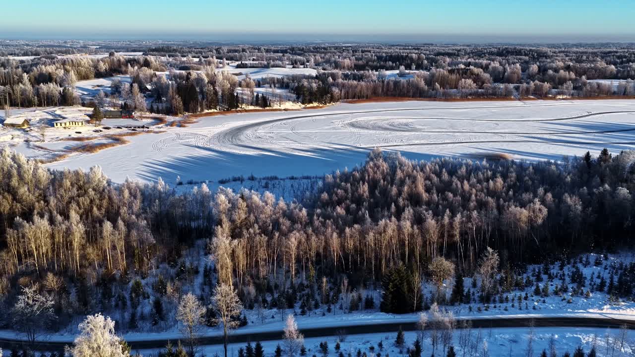 Ilmakuva jäätyneen järven kilparadasta talvisessa metsässä aamulla.