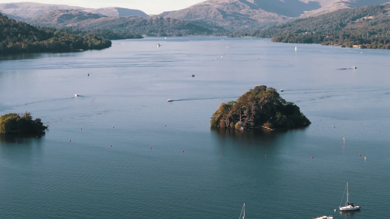 Aerial pan up over Lake Windermere, England, with islands, boats, and summer mountainscape