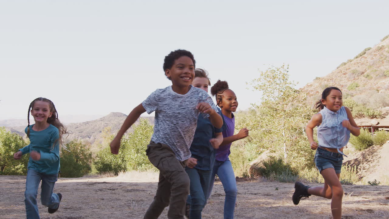 grupo de niños multiculturales con amigos corriendo hacia la cámara en el campo juntos