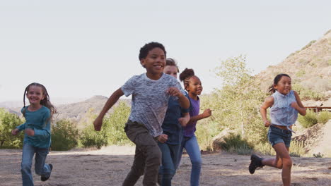 group of multi-cultural children with friends running towards camera in countryside together