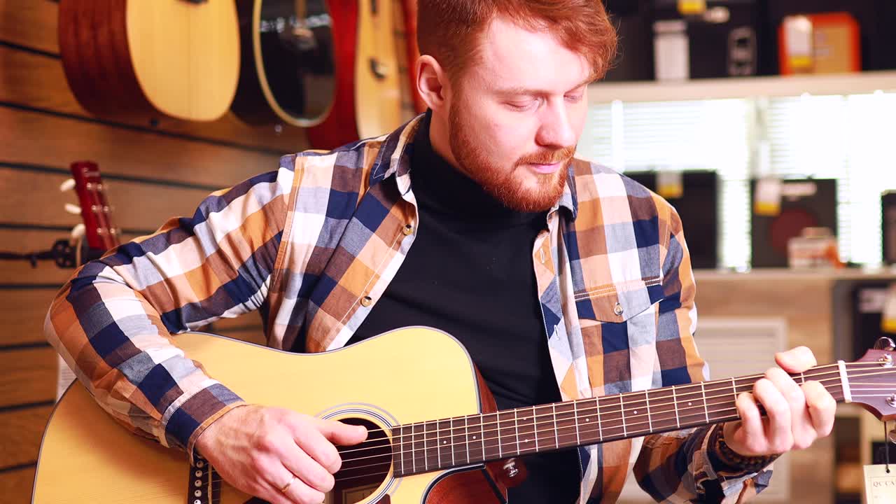 el hombre pelirrojo está eligiendo una guitarra acústica de calidad en la tienda de guitarras.