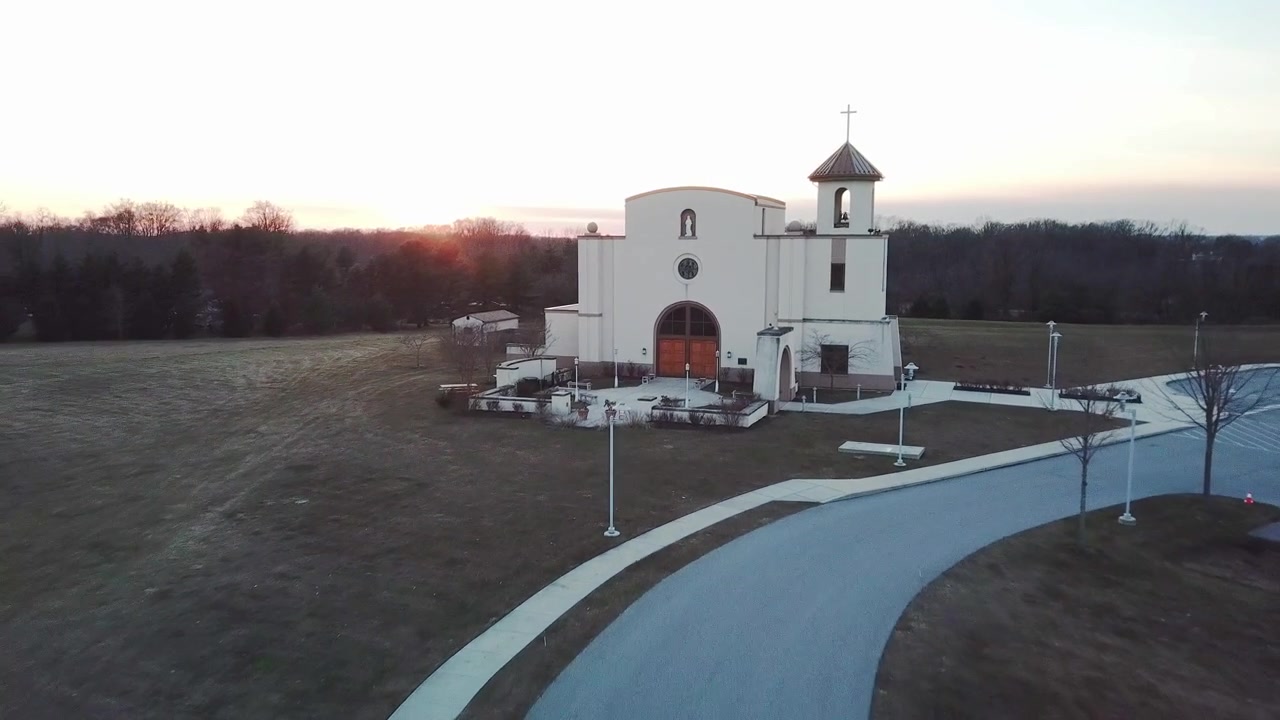 Nízko letící dron pozpátku s čelním pohledem na kostel a západem slunce v pozadí v zimní den.