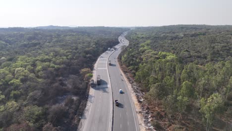aerial view of multi-lane highway winding its way through a vast, dense green forest. the road curves into the distance, with vehicles, including trucks and cars, visible as they traverse the highway