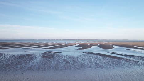 Ein-Kalter-Einsamer-Strand-Mit-Plätschernden-Wasserbecken,-Die-Zum-Meer-Führen