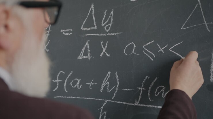 Elderly Professor Writing Equations on Chalkboard