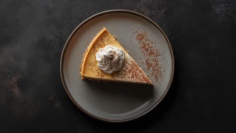 a slice of cheesecake with whipped cream and chocolate powder on a gray plate