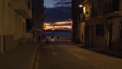 street leading to sea side during dramatic sun rise as the man walks his dog towards us