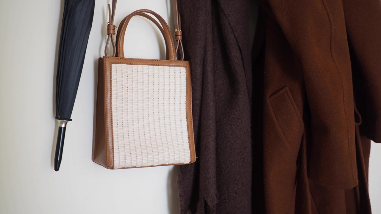 Elegante borsa intrecciata e capispalla appesi a una parete