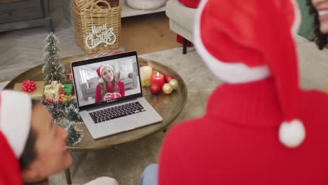 Familia-Diversa-Con-Sombreros-De-Santa-Usando-Una-Computadora-Portátil-Para-Una-Videollamada-Navideña-Con-Una-Mujer-Feliz-En-La-Pantalla