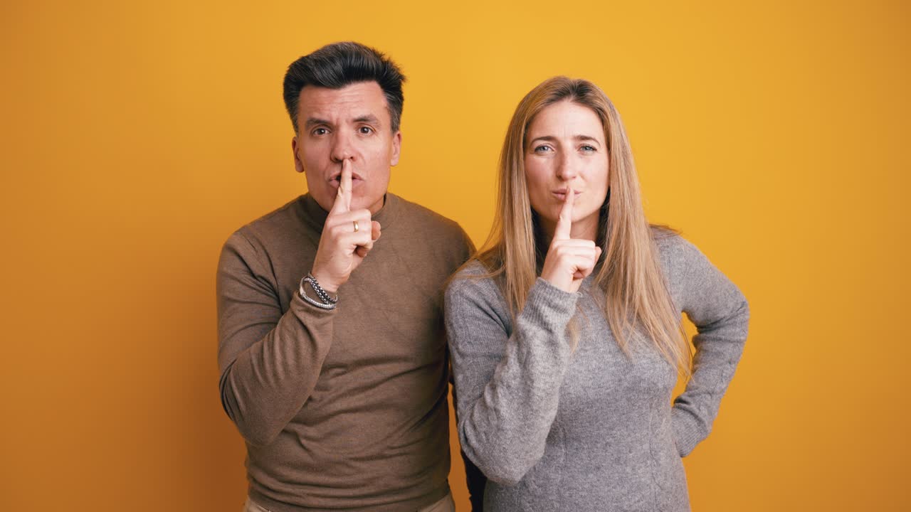 Hombre y mujer haciendo gesto de silencio sobre fondo amarillo