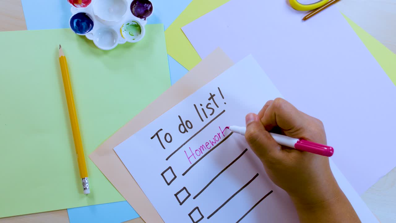 Person writes 'Homework' on to-do list with pink pen, overhead view, bright natural lighting