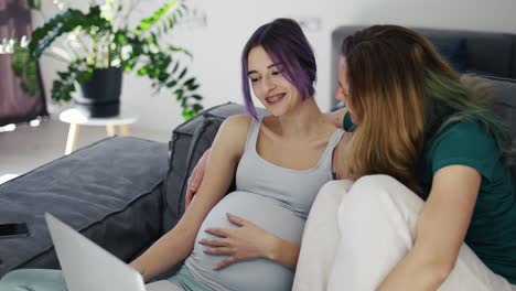 happy gay pregnant woman using laptop computer with her wife on sofa, slow motion