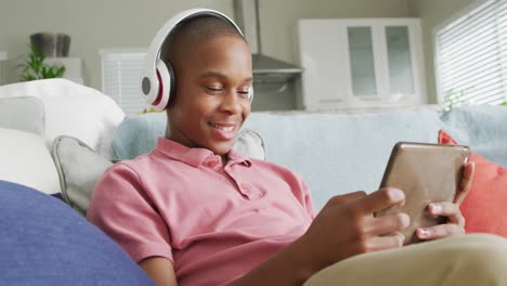 Video-of-happy-african-american-boy-in-headphones-using-tablet-on-sofa