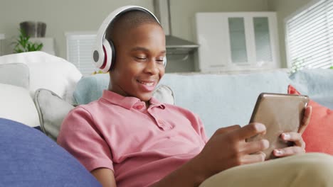 Video-De-Un-Niño-Afroamericano-Feliz-Con-Auriculares-Usando-Una-Tableta-En-El-Sofá