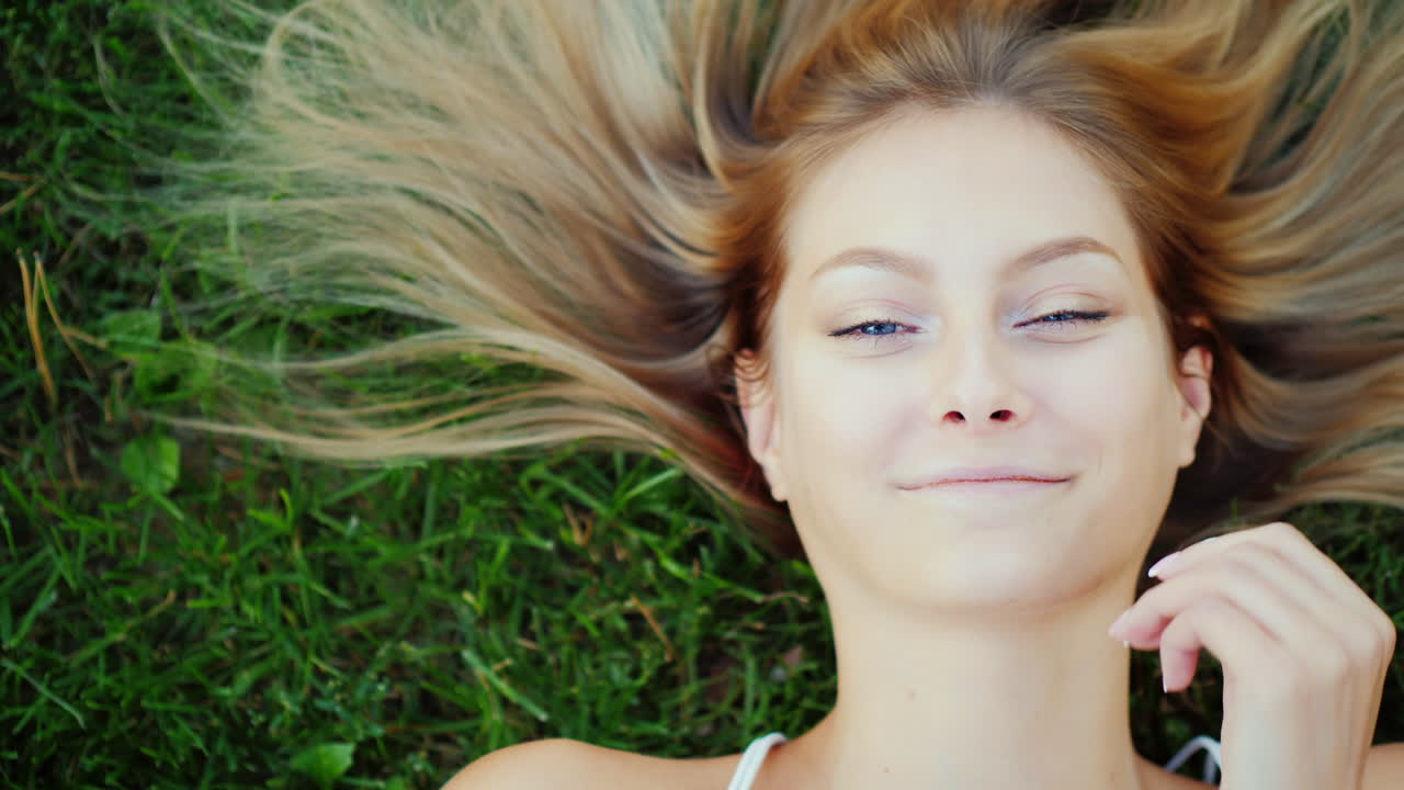 Ritratto di una giovane donna con i capelli lunghi. Lei giace sul prato, i suoi capelli sono splendidamente distesi sull'erba.