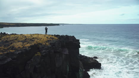 Plano-General-Del-Hombre-Tomando-Fotos-De-Las-Olas-Desde-Un-Acantilado-En-Islandia