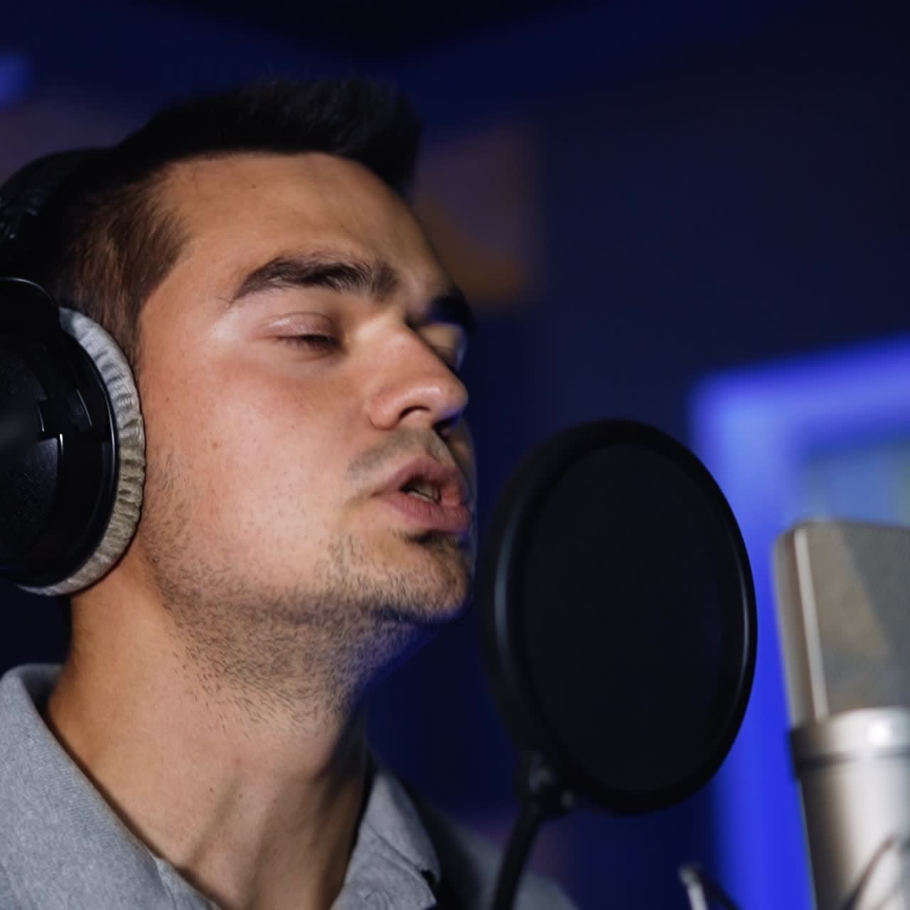 Un cantante che registra una canzone in studio. Un artista maschile in piedi davanti al microfono professionale e con le cuffie