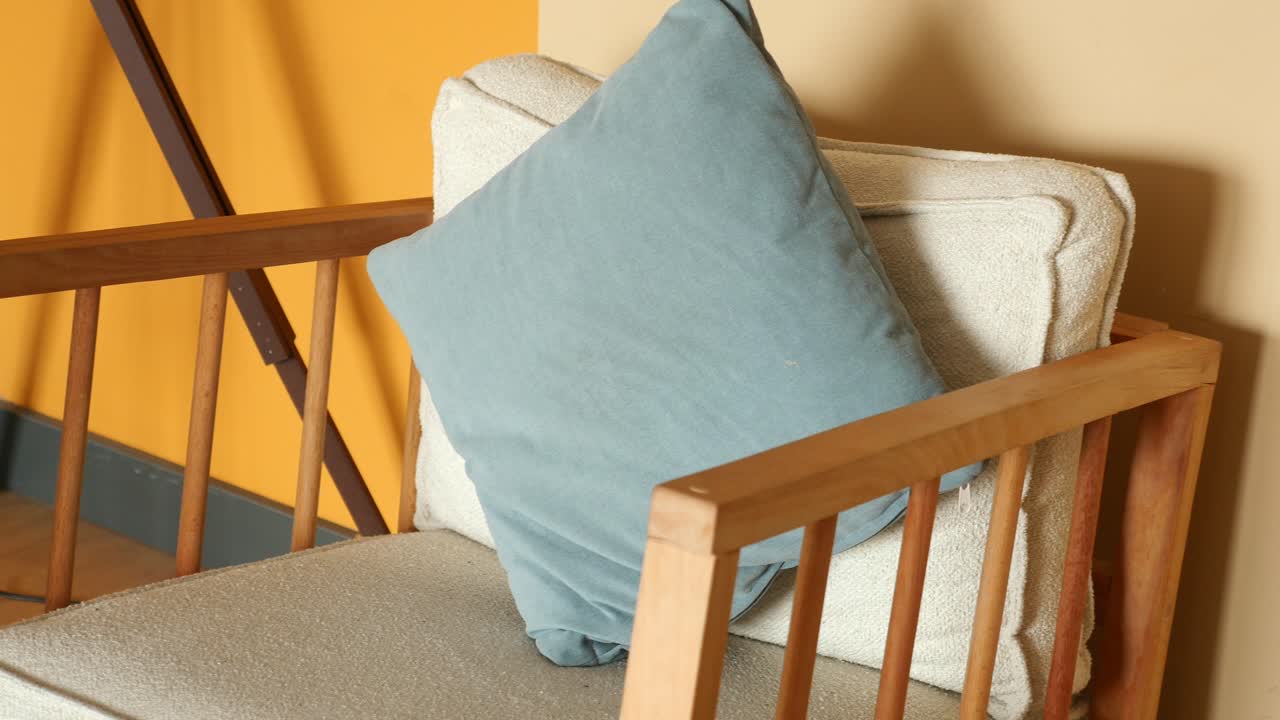 sillón de madera con cojín y almohada de color claro