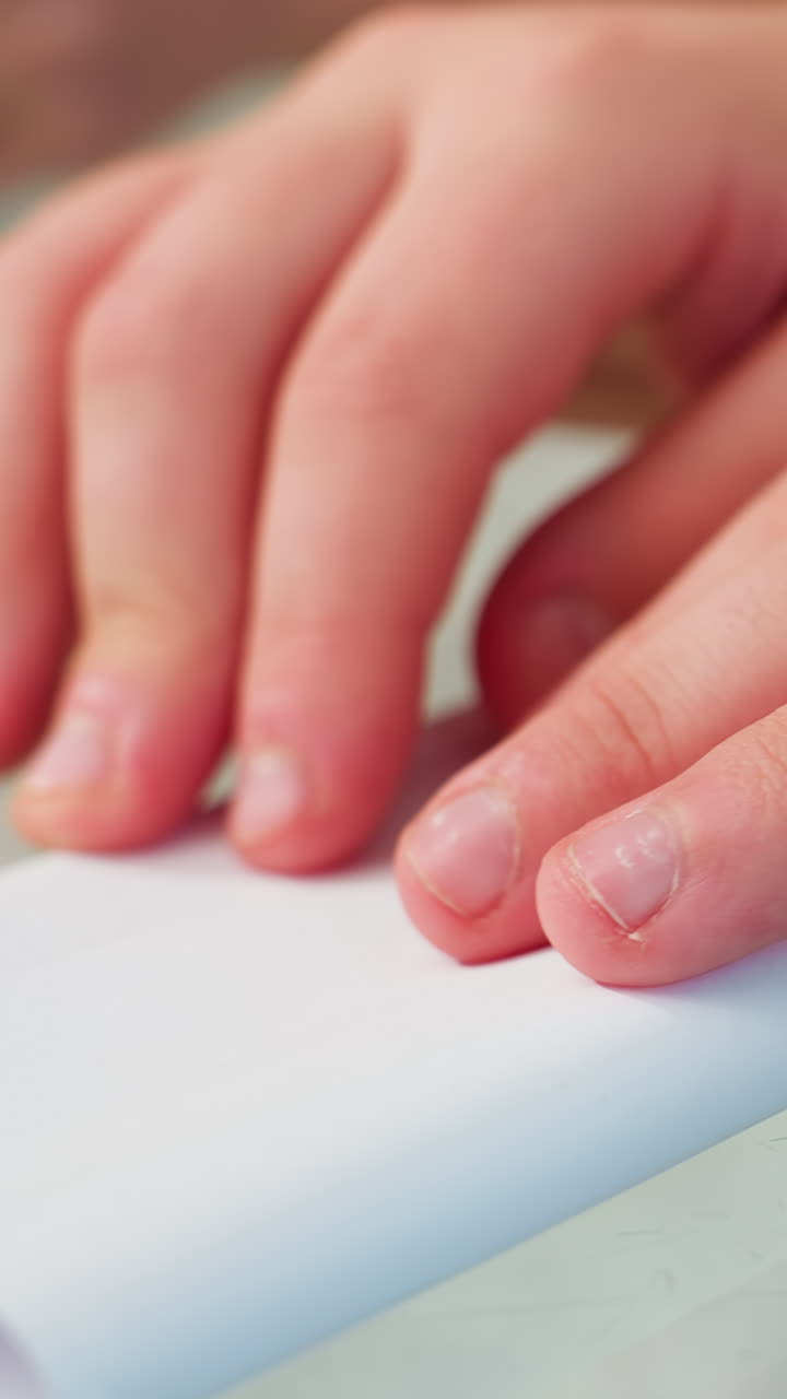 primer plano de las manos de un niño caucásico enrollando papel para formar un tubo sobre una mesa reflectante experimentación lúdica creando un modelo diminuto y practicando el control de la motricidad fina juego imaginativo y aprendizaje práctico