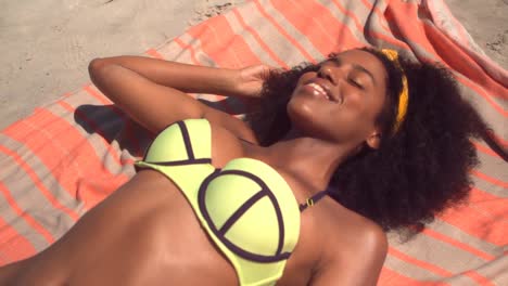 beautiful young african american woman in green bikini relaxing on blanket at beach in